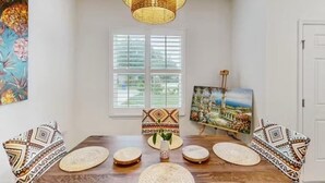 A dining area with a wooden table, woven placemats, patterned cushions, a hanging light fixture, and artwork on the walls. - Boaters Cove ~ 3 Car Garage Home (Sebastian)