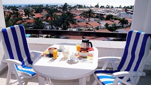 A balcony with two striped chairs, a table with breakfast items, and a view of a coastal town. - Tamaran (San Bartolomé de Tirajana)