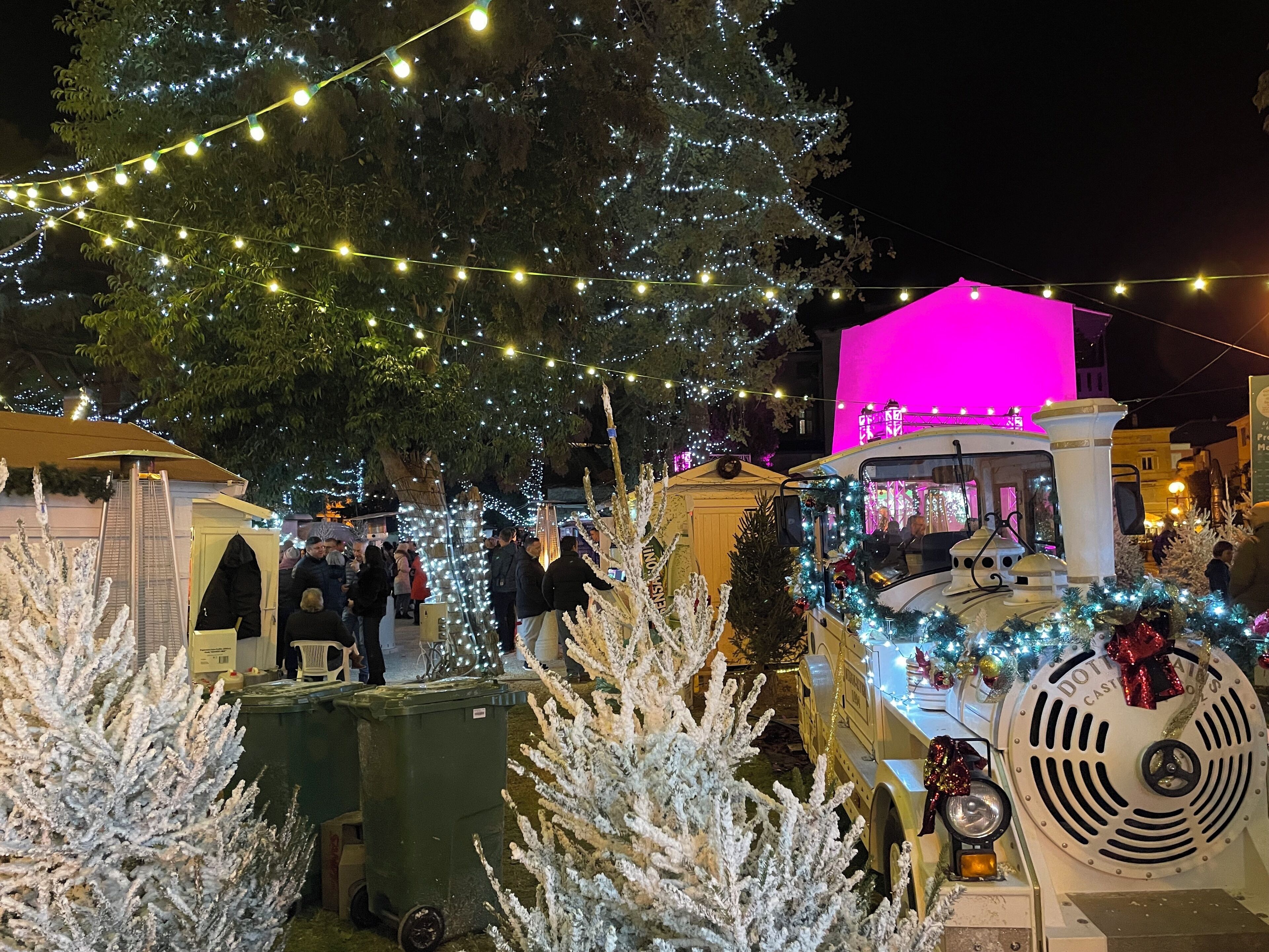 A festive outdoor market with illuminated trees and a vintage tram.