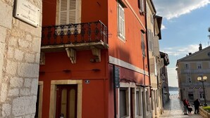 Una estrecha calle adoquinada flanqueada por edificios históricos, destacando un edificio rojo con contraventanas blancas y un balcón.