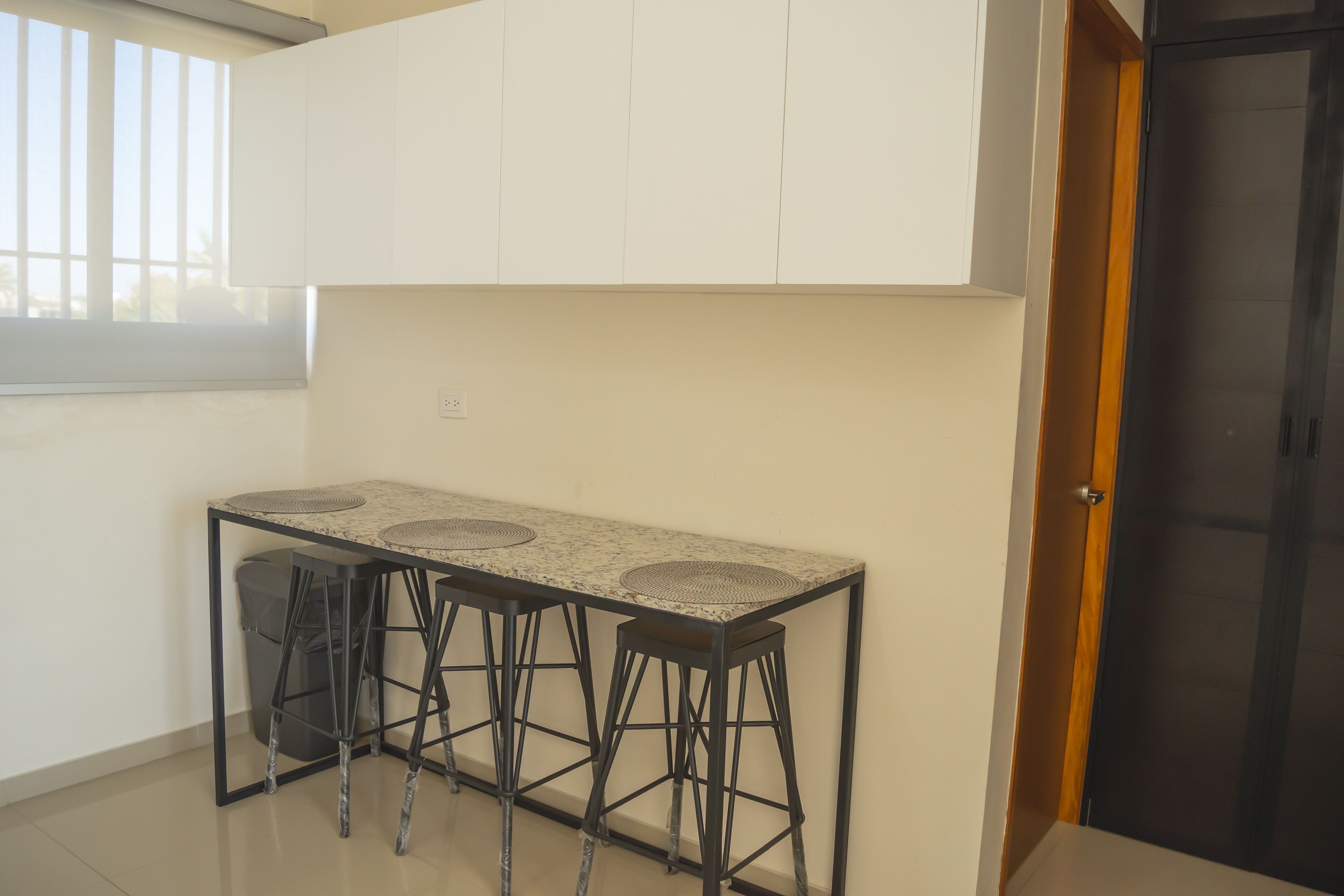 Una cocina con mostrador blanco, taburetes negros y una puerta negra.