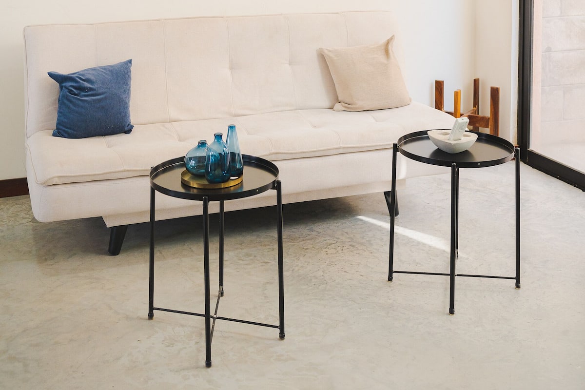 A modern living room with a white sofa, two black tables, a flat-screen TV, and a unique light fixture.