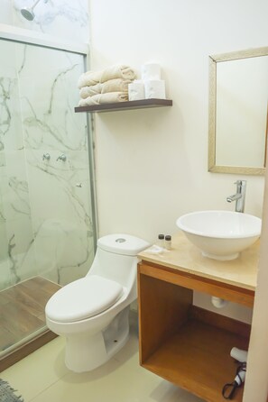 A bathroom with a toilet, sink, and shower. There is a shelf with towels and toiletries. - Soho Apartments (Mazatlán)