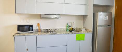 A kitchen with white cabinets, a microwave, a stainless steel refrigerator, and a granite countertop.