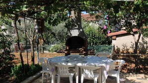 An outdoor patio with a round table and white plastic chairs, surrounded by greenery and a stone wall. - Charming 2-Bedroom Haven for Four, No Pets (Pula)