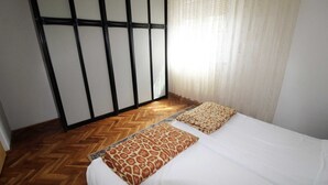 A bedroom with a bed, a patterned throw pillow, a herringbone-patterned floor, and a sliding door with a black frame. - Charming 2-Bedroom Haven for Four, No Pets (Pula)