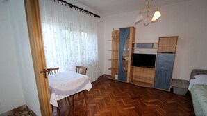 A room with a wooden herringbone floor, a dining table with chairs, a television on a stand, and a bed. - Charming 2-Bedroom Haven for Four, No Pets (Pula)