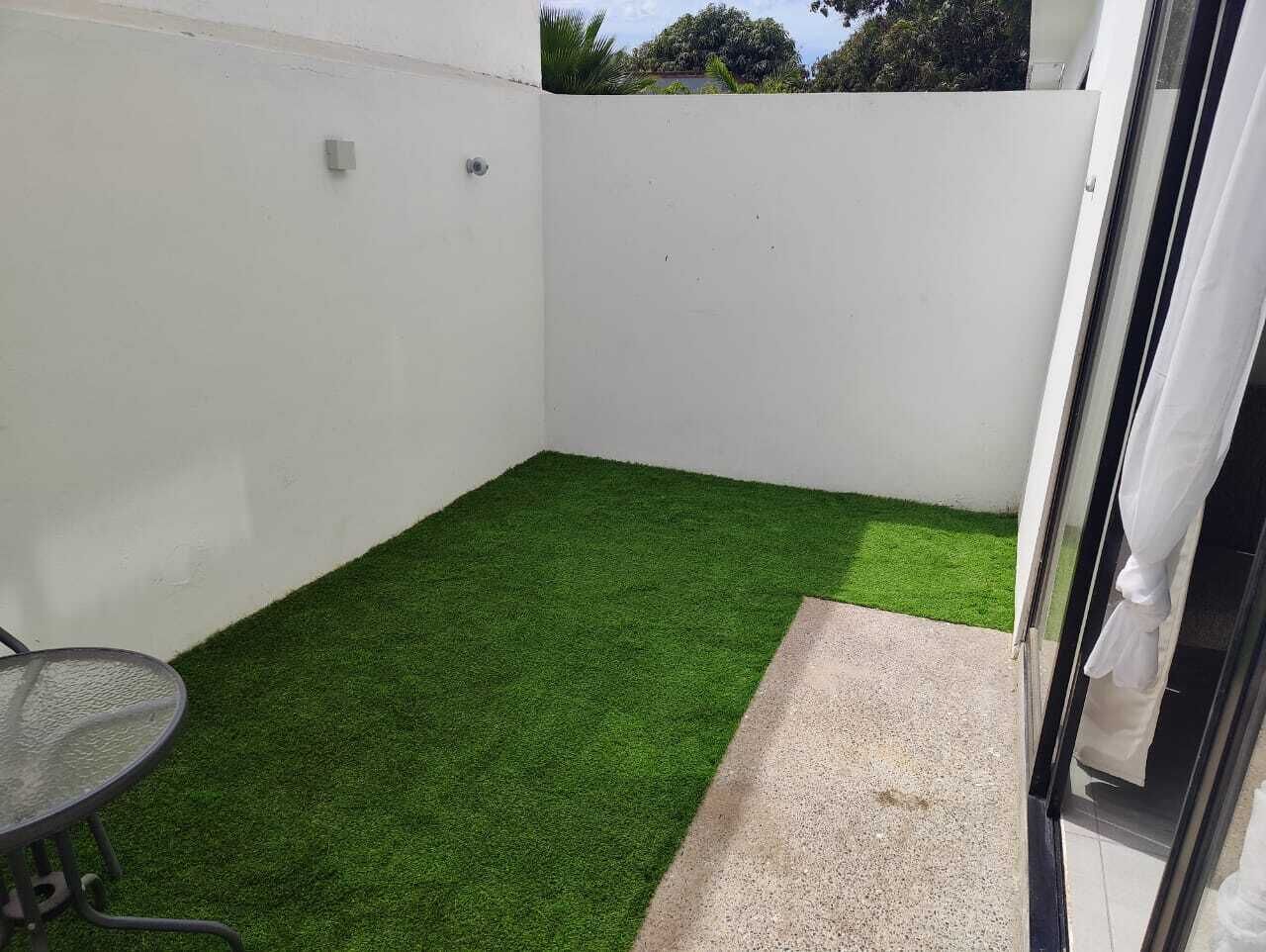 Un pequeño patio amurallado con césped artificial verde, una mesa de metal y un escalón de hormigón que lleva a una puerta.