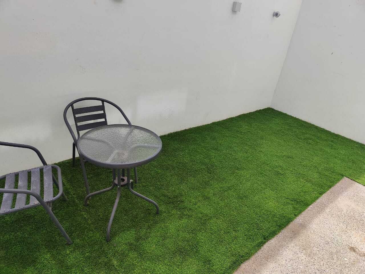 Un pequeño patio con una mesa redonda y dos sillas, rodeado de césped artificial.