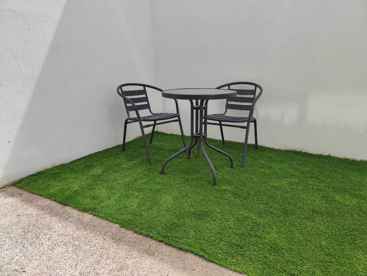 A small outdoor seating area with a round table and two chairs, surrounded by artificial grass.