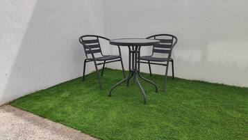 A small outdoor seating area with a round table and two chairs, surrounded by artificial grass.