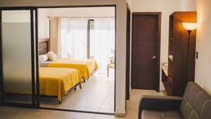 Habitación de hotel con dos camas, un sofá, una lámpara y una puerta que da a un baño.