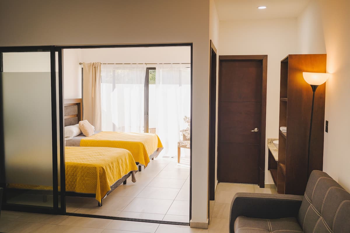 A hotel room with two beds, a sofa, a lamp, and a door leading to a bathroom.