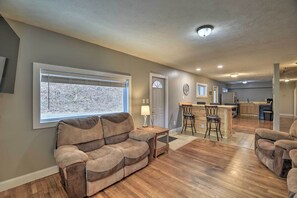 A spacious living room with a large window, a sofa, and a kitchen area in the background. - Mullens Cabin w/ Gas Grill & Mountain Views! (Mullens)