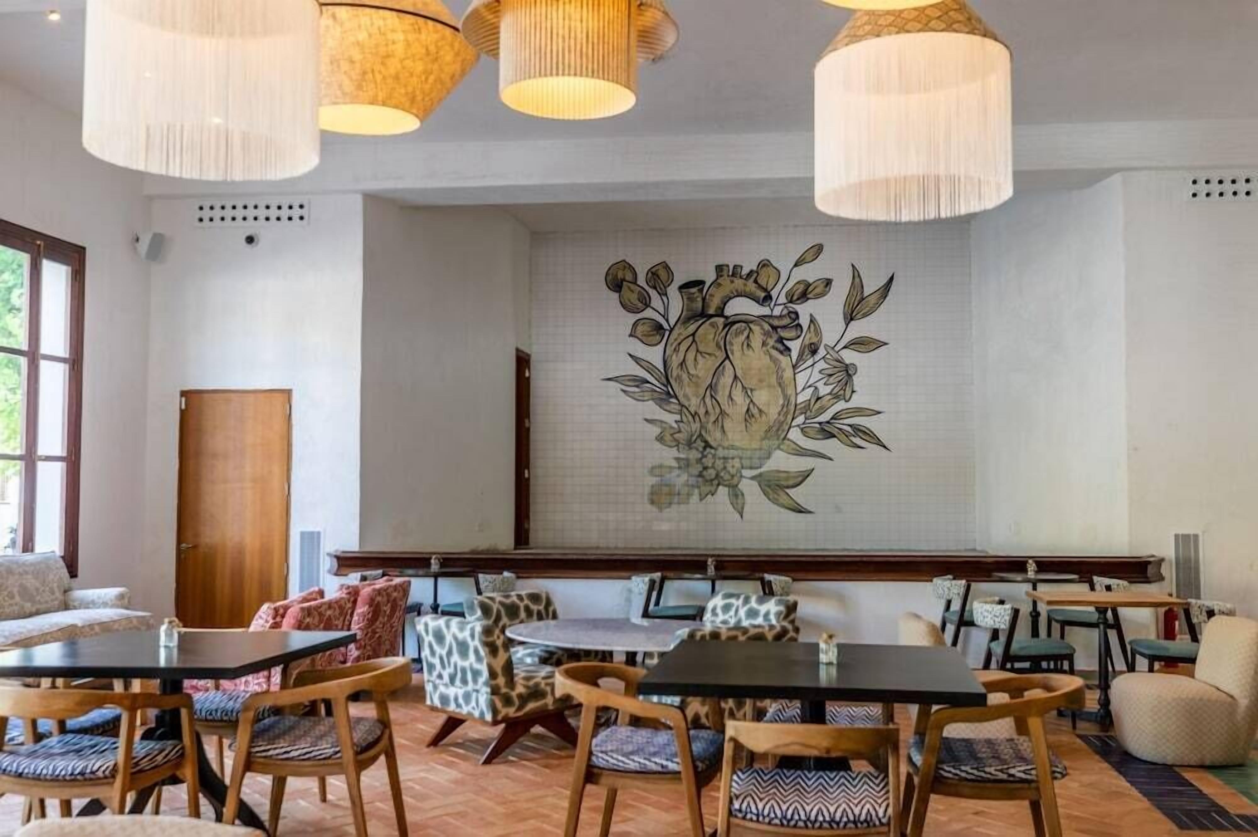 A dining area with wooden tables and chairs, a large wall mural, and hanging pendant lights.