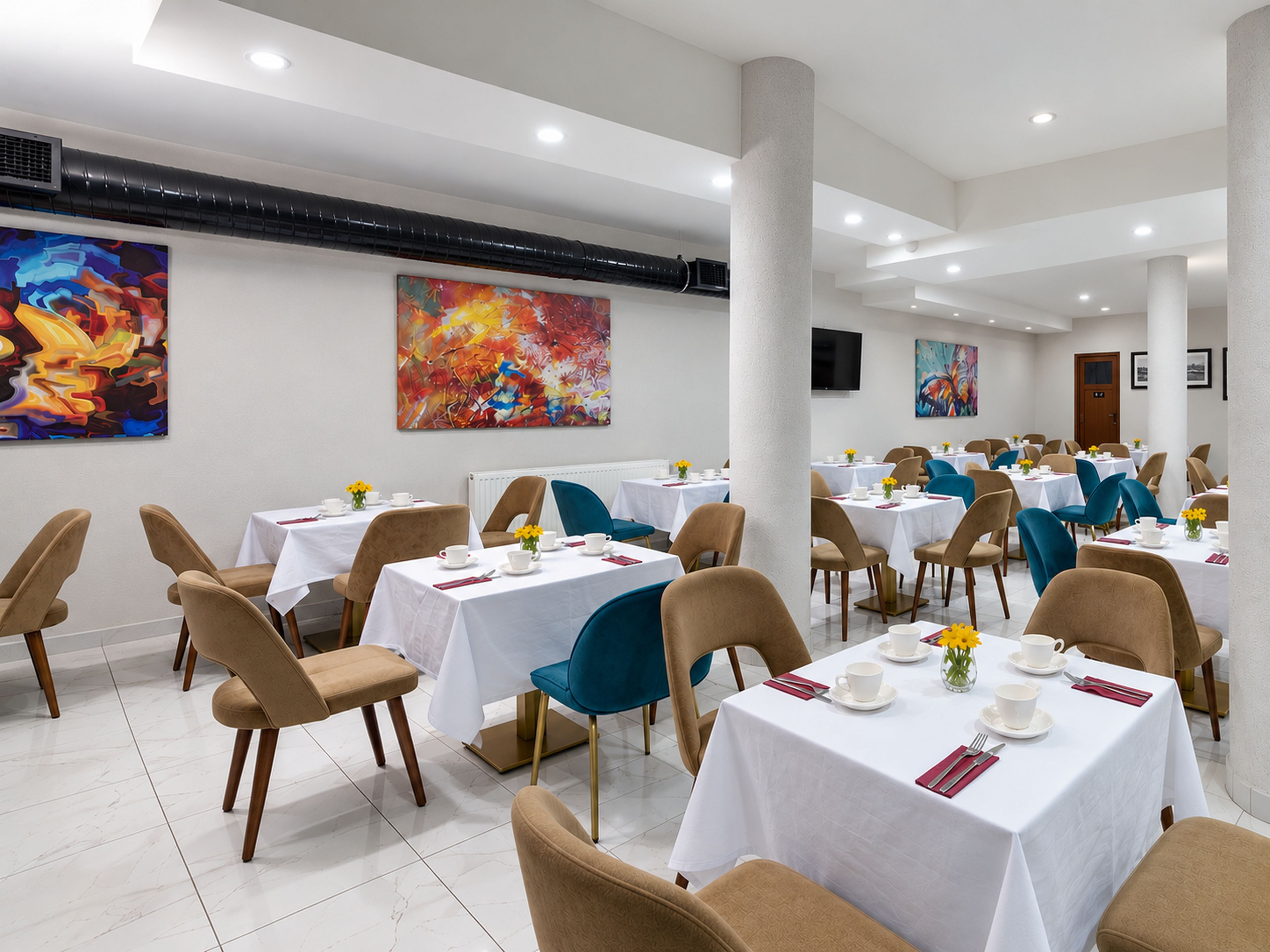 A dining area with multiple tables and chairs, white tablecloths, and artwork on the walls.