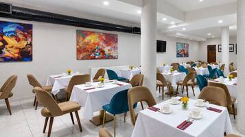 A dining area with multiple tables and chairs, white tablecloths, and artwork on the walls.