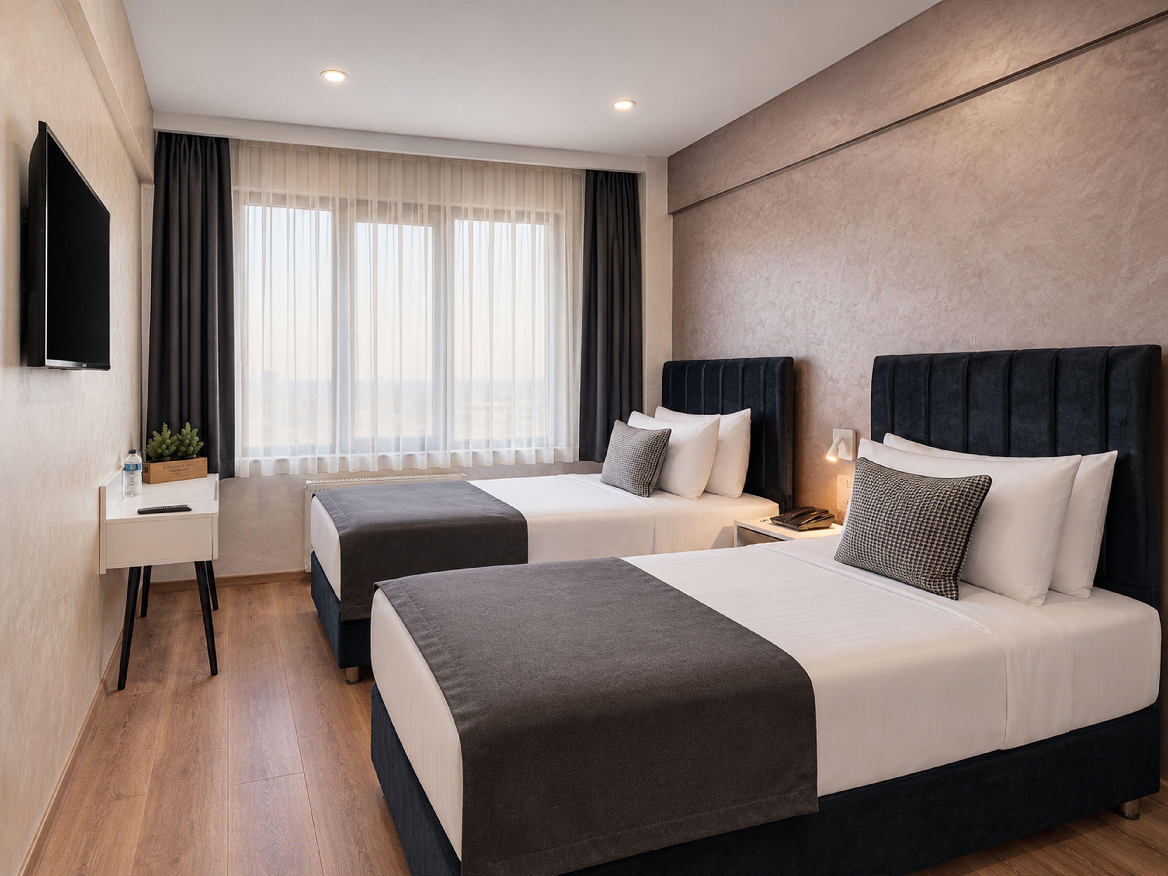 A hotel room with two beds, a desk, a TV, and a window with curtains.