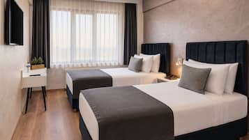 A hotel room with two beds, a desk, a TV, and a window with curtains.