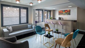 Una habitación de hotel moderna con sofá, sillas, una mesita, zona de bar y ventanas amplias.