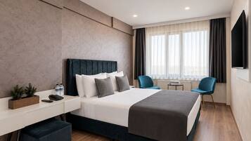 A modern hotel room with a bed, bedside tables, a desk, a chair, and a TV.