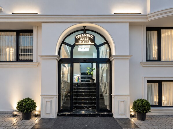 The entrance to the Istanbul Efes Hotel with a glass door and a staircase leading inside.