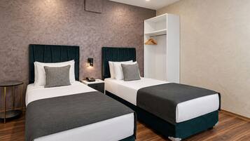 A hotel room with two beds, a wardrobe, a bedside table, and a wall-mounted light.