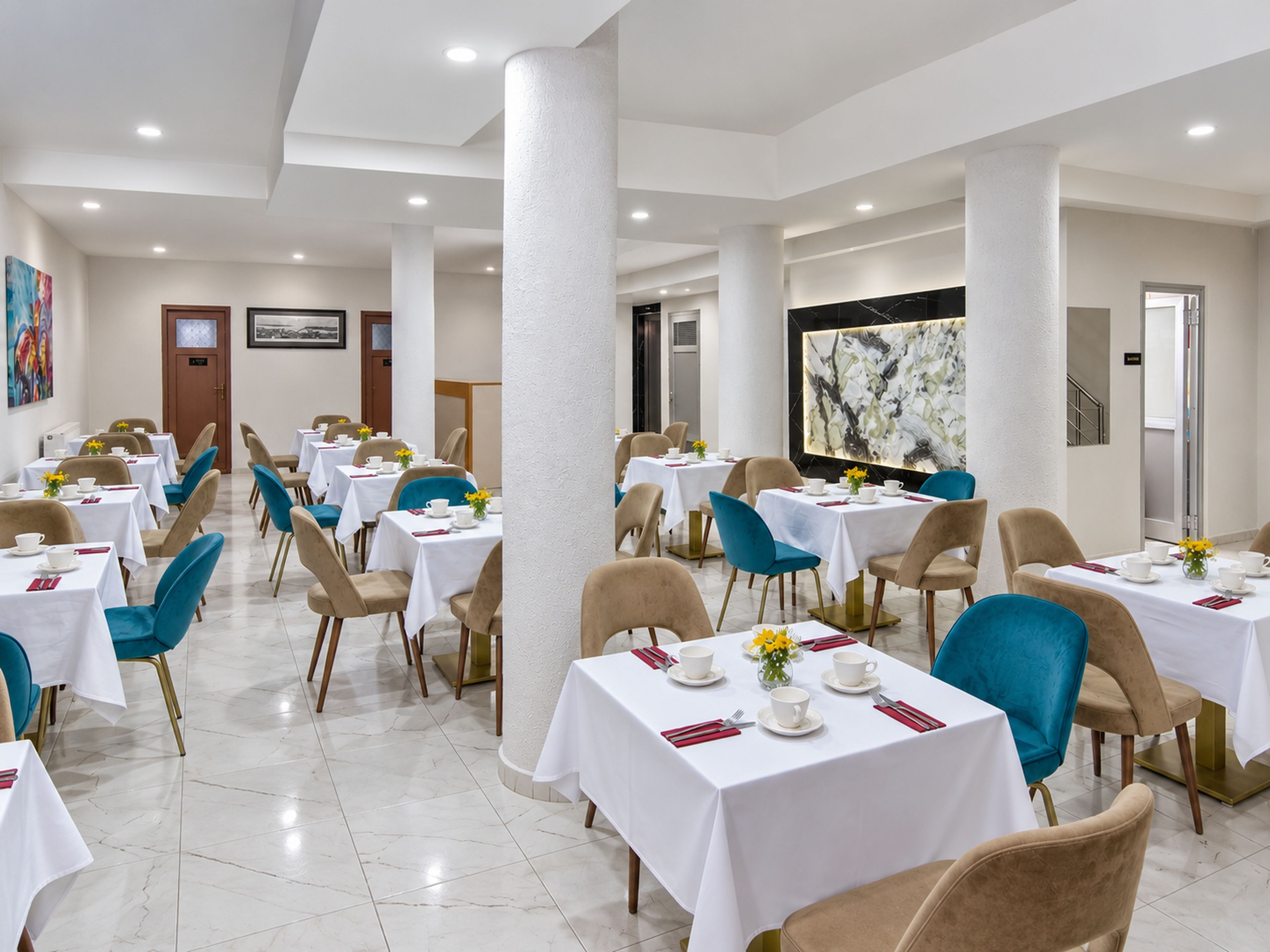 A hotel dining area with multiple tables and chairs, a large abstract painting on the wall, and a door in the background.