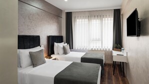 Habitación de hotel con dos camas, un escritorio, un televisor y una ventana con cortinas.