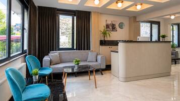 A modern hotel room with a sofa, chairs, a small table, and a kitchen area.