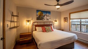 Une chambre à coucher avec un lit, un ventilateur de plafond, une fenêtre et un tableau accroché au mur.