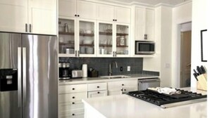 A modern kitchen with white cabinetry, a stainless steel refrigerator, a microwave, and a gas stove.
