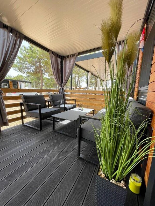 An outdoor seating area with a wooden deck, black furniture, and a large plant. - D&I mobile home - Mobile Home with Terrace (Privlaka)