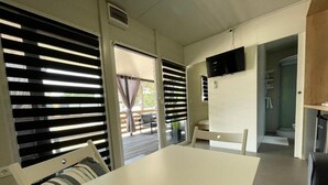 A compact room with a white table and chairs, a flat-screen TV mounted on the wall, and a sliding door leading to an outdoor area with a patio. - D&I mobile home - Mobile Home with Terrace (Privlaka)