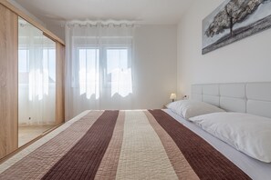 A bedroom with a large bed, a bedside table, a nightstand, and a painting on the wall. - Modern two bedroom apartment with shared pool (Zadar)