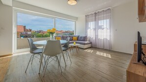 Ein modernes Wohnzimmer mit Essbereich, großen Fenstern und Blick auf Gebäude.
