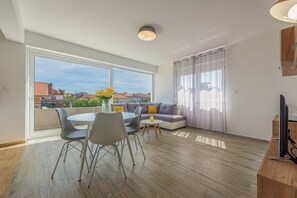 Uma sala de estar moderna com área de jantar, janelas amplas e vista para edifícios.