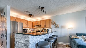 A modern kitchen with a central island, wooden cabinets, and a stainless steel refrigerator. - Elegant Beach Escape, Warm, Comfy Cozy, Family fun, Massage Chair, Retro Games (North Topsail Beach)
