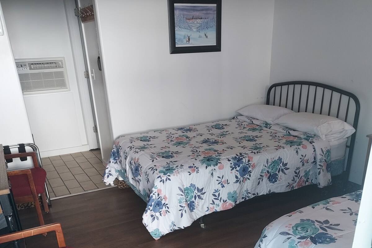 A bedroom with two single beds, a wooden chair, a small table, and a framed picture on the wall.