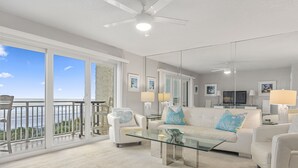 A spacious living room with a glass coffee table, white sofas, and a large sliding glass door leading to a balcony with a view of the ocean. - Gorgeous Condo with Ocean Views in St. Augustine (St. Augustine)