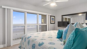 A bedroom with a large bed, a ceiling fan, a TV, and a view of the beach through large windows. - Gorgeous Condo with Ocean Views in St. Augustine (St. Augustine)