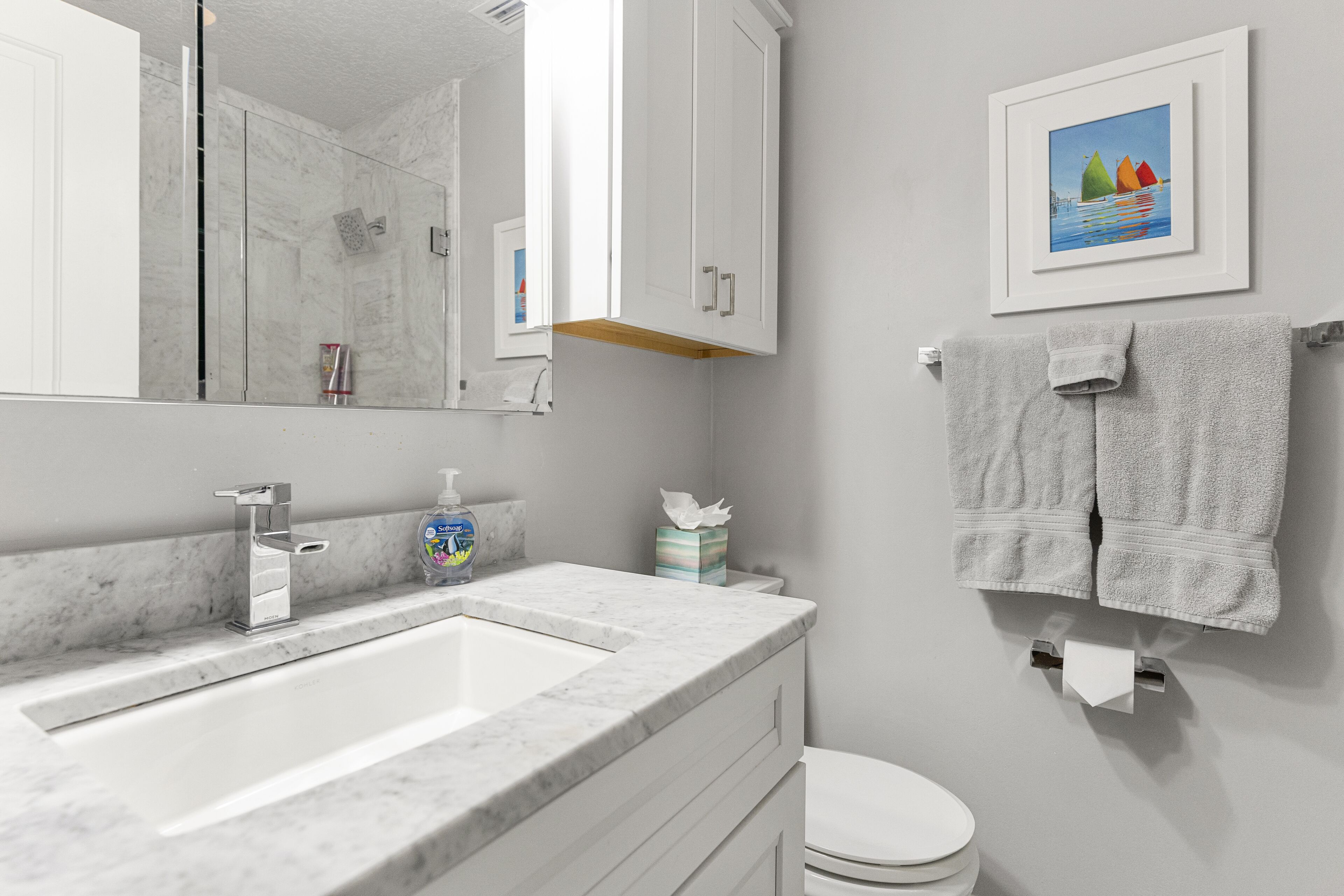 Un bagno con un lavabo in marmo, un water, un portasciugamani con asciugamani, un quadro appeso alla parete e uno specchio.