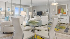 A modern dining area with a glass table, white chairs, and a large mirror reflecting the room. - Gorgeous Condo with Ocean Views in St. Augustine (St. Augustine)