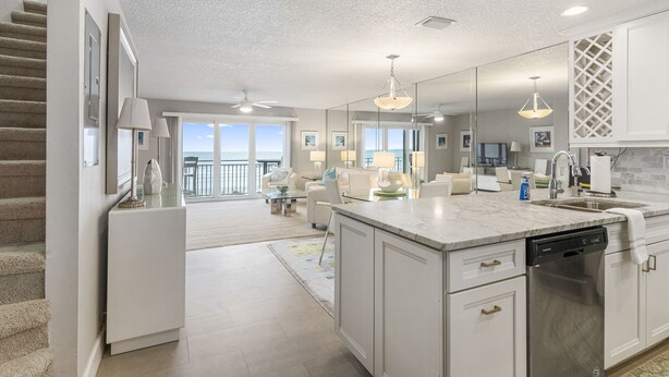 A modern kitchen with white cabinetry, a marble countertop, and a dishwasher. There is a large window providing a view of the outdoors. - Gorgeous Condo with Ocean Views in St. Augustine (St. Augustine)