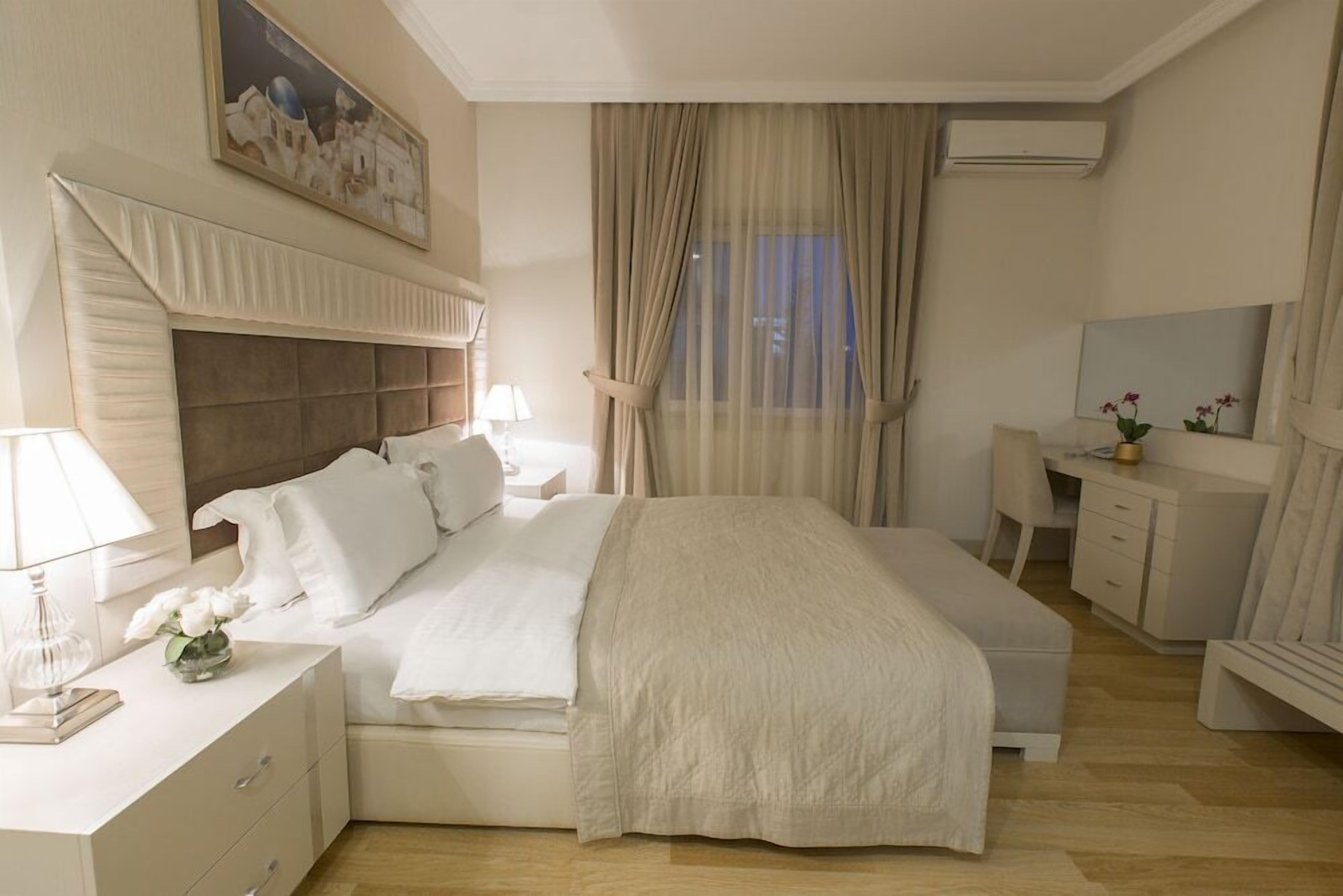 A hotel room with a bed, bedside tables, a desk, a chair, and a window with curtains.