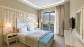 A hotel room with a large bed, a TV, a bedside table with a lamp, and a view of the outdoors. - Gabala Garden Hotel (Gabala)