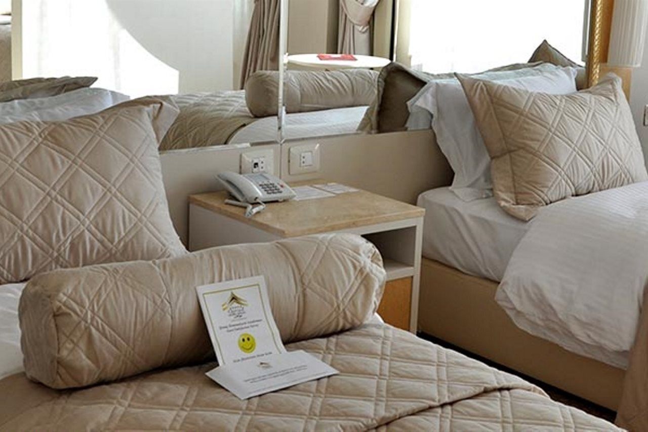 A hotel room with multiple beds, a bedside table with a phone, and a certificate on the bed.