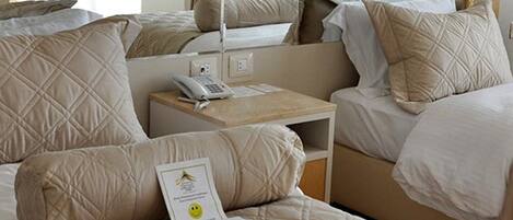 A hotel room with multiple beds, a bedside table with a phone, and a certificate on the bed.