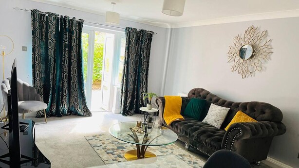 A modern living room with a glass coffee table, a leather sofa with cushions, a television, and a decorative wall piece. - Lovely 2-bed House in Rochester (Rochester)