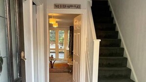 A hallway with a staircase, a sign reading "THIS IS OUR HAPPY PLACE", and a door with a glass panel. - Lovely 2-bed House in Rochester (Rochester)